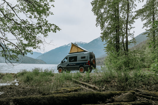 A Super Pacific Cloud Cap™ pop-top installed on a camper van, shown parked in a scenic forest setting. The sleek, low-profile design integrates seamlessly with the van roof, featuring a 4-season tent ideal for overlanding, road trips, and off-grid camping
