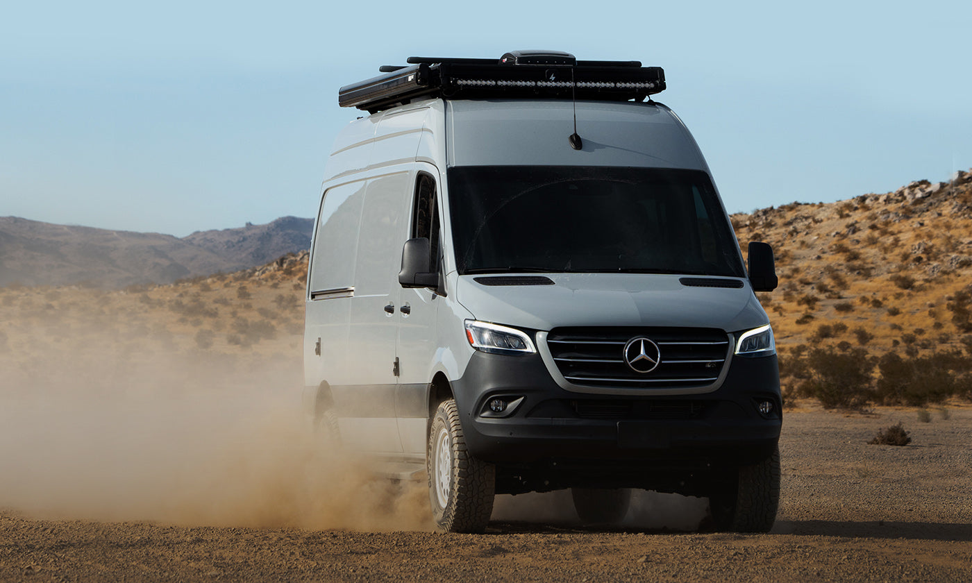 A Mercedes Sprinter Van with CloudCap poptop van tent and Baja Designs lightbar and Nomad wheels drives through the desert.