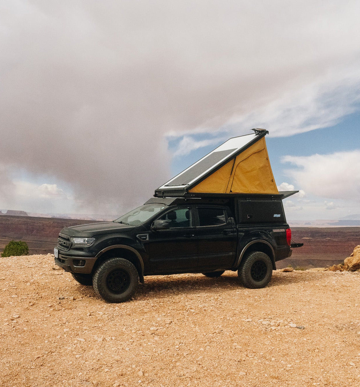 Black Ford Ranger with Super Pacific X1 Camper parked on a rocky outcrop under a cloudy sky.
