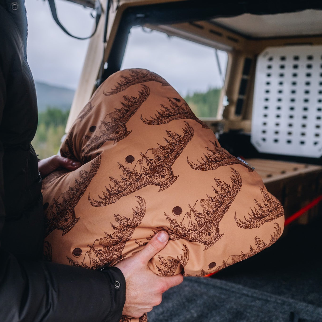 Man holding a HEST x Super Pacific custom pillowcase in front of a Super Pacific truck bed camper.