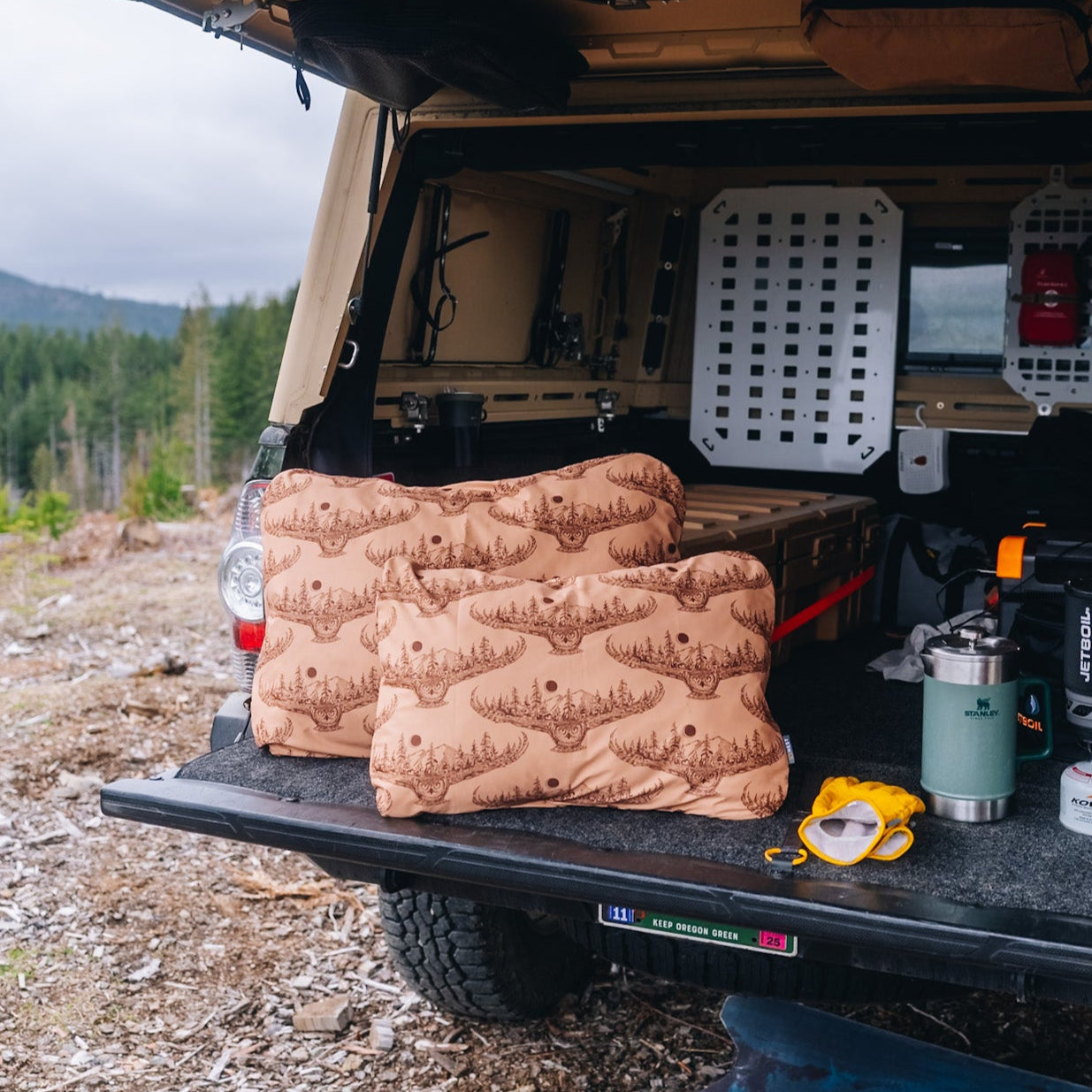Two HEST x Super Pacific custom pillowcases sitting on the tailgate of a Toyota Tacoma with a Super Pacific truck bed camper.