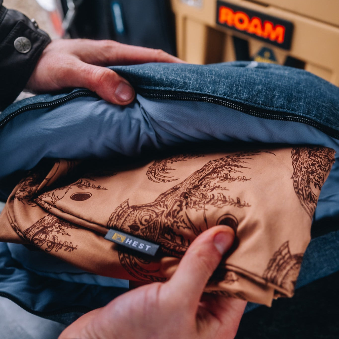 A man opening a HEST camp pillow to reveal a HEST x Super Pacific custom pillowcase.