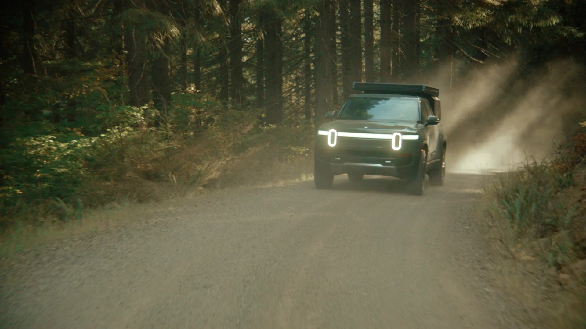 All-electric Rivian R1T overland rig with Super Pacific X1 Camper driving off-road on rugged backcountry trail.