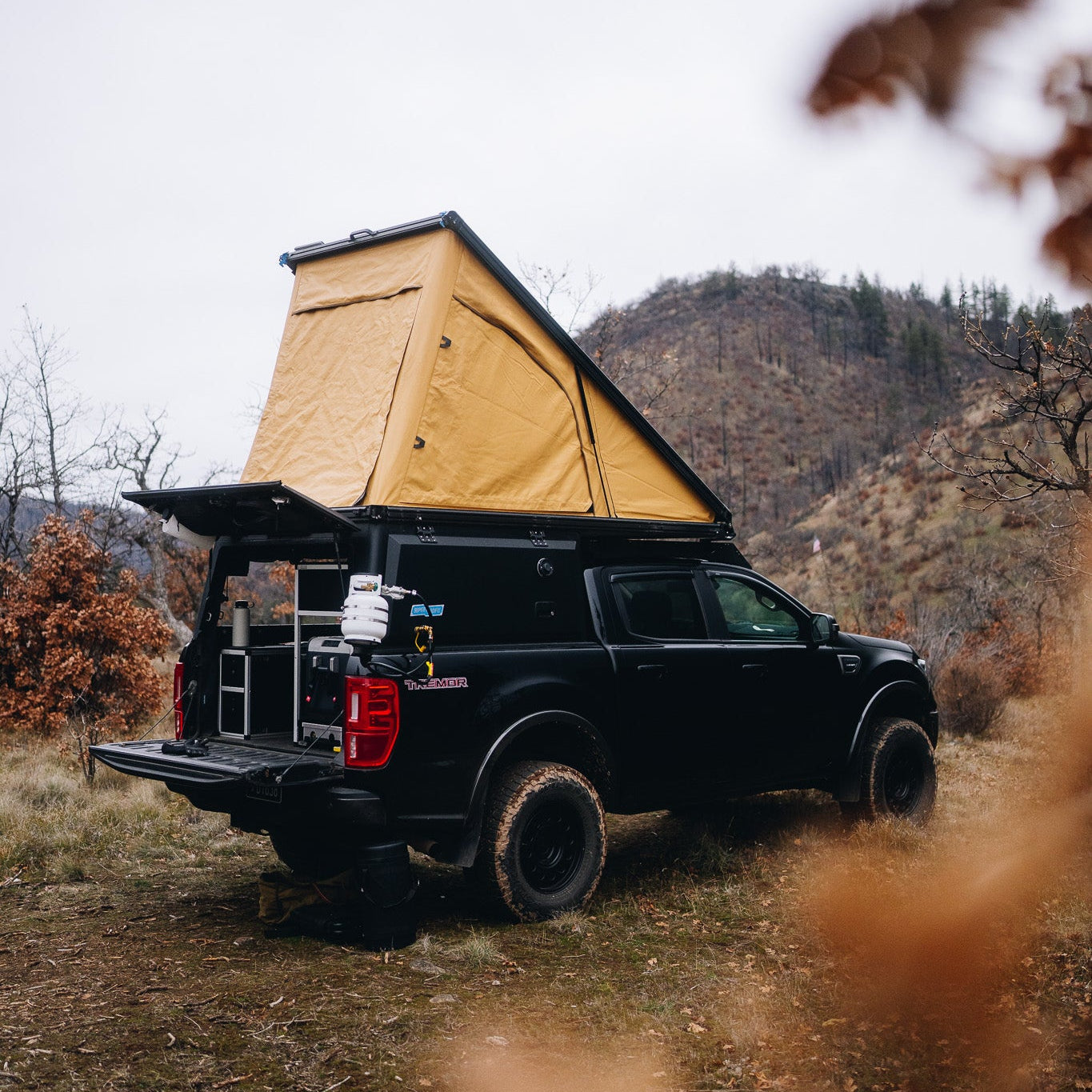 Black Ford Ranger Truck with propane tank attached to the back of a Super Pacific X1 Camper with a forest background.