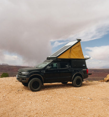 Black Ford Ranger with Super Pacific X1 Camper parked on a rocky outcrop under a cloudy sky.