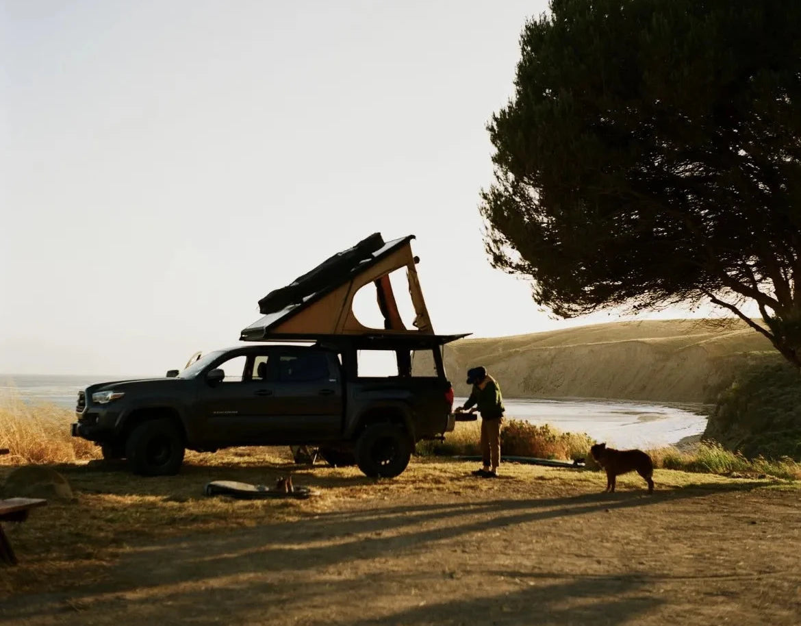 A Toyota Tacoma pickup truck parked near a beach, with a Super Pacific X1 Camper.