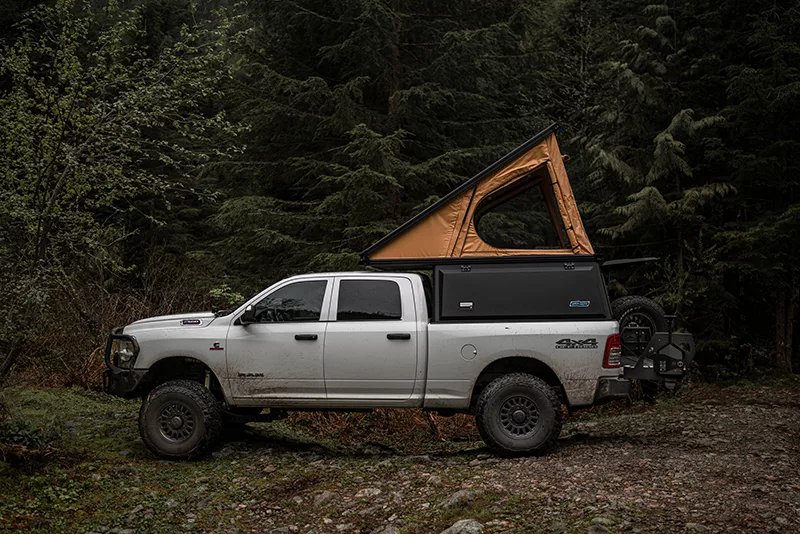 Ram 2500 truck parked in a forest with a Super Pacific X1 Camper mounted to the truckbed.