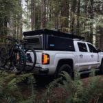 Chevy Silverado parked in a forest with Super Pacific X1 camper and mountain bikes mounted to the truckbed.